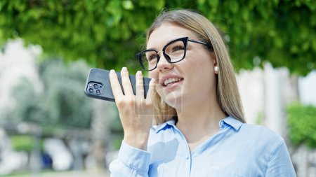 Téléchargez les photos : Jeune femme blonde d'affaires envoyant un message vocal par smartphone souriant au parc - en image libre de droit