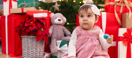 Photo for Adorable hispanic baby holding hoop toy sitting on floor by christmas tree at home - Royalty Free Image