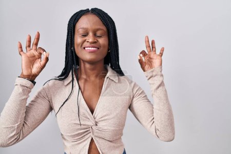 Photo for African woman with braids standing over white background relaxed and smiling with eyes closed doing meditation gesture with fingers. yoga concept. - Royalty Free Image