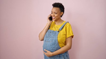 Foto de Mujer embarazada joven hablando en teléfono inteligente sonriendo sobre el fondo rosa aislado - Imagen libre de derechos