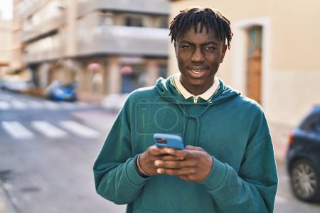 Foto de Hombre afroamericano sonriendo confiado usando smartphone en la calle - Imagen libre de derechos