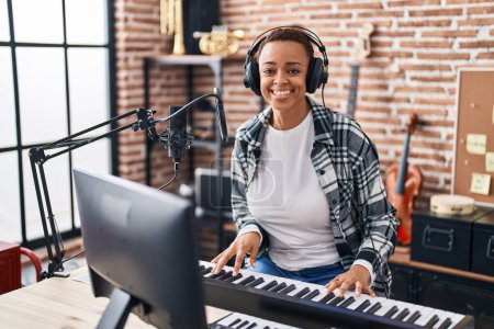 Foto de Mujer afroamericana músico sonriendo confiado tocando el piano en el estudio de música - Imagen libre de derechos