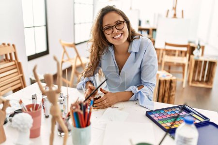 Téléchargez les photos : Jeune belle hispanique femme artiste souriant confiant faire pot en céramique avec les mains au studio d'art - en image libre de droit