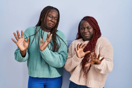 Foto de Dos mujeres africanas de pie sobre fondo azul expresión disgustada, disgustadas y temerosas haciendo repugnancia cara porque la reacción de aversión. - Imagen libre de derechos
