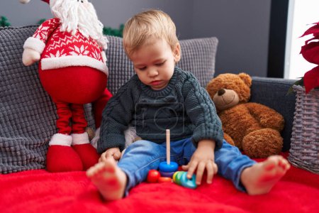 Foto de Adorable niño rubio jugando con aros de juguete sentado en el sofá por la decoración de Navidad en casa - Imagen libre de derechos