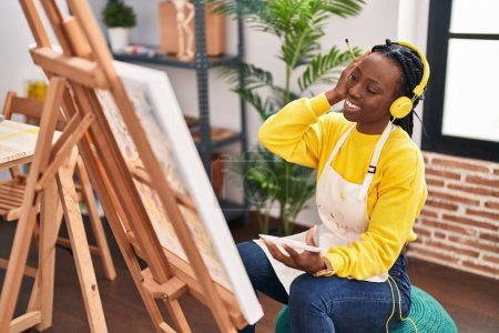 Téléchargez les photos : African american woman artist listening to music drawing at art studio - en image libre de droit