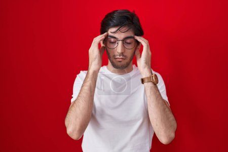 Photo for Young hispanic man standing over red background with hand on head, headache because stress. suffering migraine. - Royalty Free Image