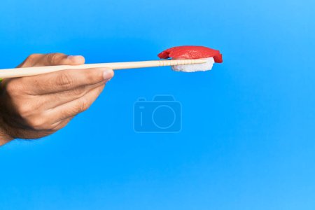Photo for Hand of man holding tuna nigiri with chopsticks over isolated blue background - Royalty Free Image
