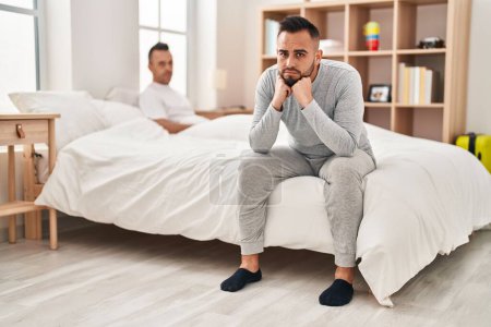 Téléchargez les photos : Deux hommes couple assis sur le lit avec expression malheureuse dans la chambre - en image libre de droit