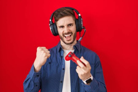 Photo for Hispanic man with beard playing video game holding controller screaming proud, celebrating victory and success very excited with raised arms - Royalty Free Image