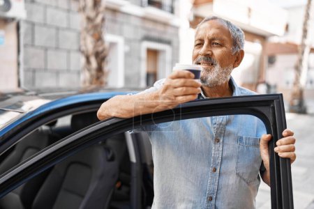 Téléchargez les photos : Homme âgé aux cheveux gris buvant du café debout en voiture dans la rue - en image libre de droit