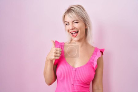 Photo for Young caucasian woman standing over pink background doing happy thumbs up gesture with hand. approving expression looking at the camera showing success. - Royalty Free Image