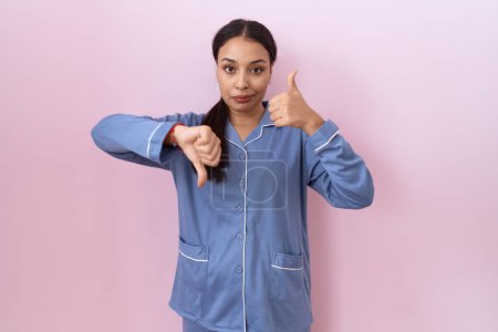 Photo for Young arab woman wearing blue pajama doing thumbs up and down, disagreement and agreement expression. crazy conflict - Royalty Free Image