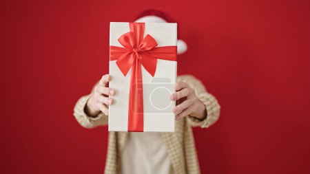 Photo for Young hispanic man holding christmas gift over isolated red background - Royalty Free Image