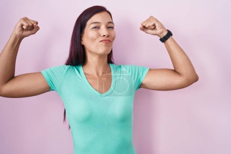 Foto de Mujer hispana joven de pie sobre fondo rosa mostrando los músculos de los brazos sonriendo orgulloso. concepto de fitness. - Imagen libre de derechos