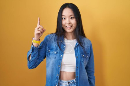 Photo for Young asian woman standing over yellow background pointing finger up with successful idea. exited and happy. number one. - Royalty Free Image