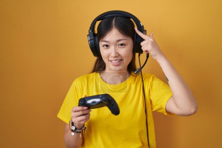 Foto de Chino joven mujer jugando videojuego celebración controlador sonriendo apuntando a la cabeza con un dedo, gran idea o pensamiento, buena memoria - Imagen libre de derechos