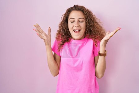 Foto de Young caucasian woman standing over pink background celebrating crazy and amazed for success with arms raised and open eyes screaming excited. winner concept - Imagen libre de derechos
