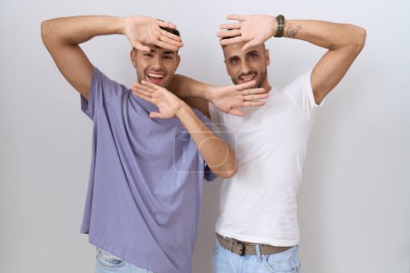 Téléchargez les photos : Couple homosexuel gay debout sur fond blanc souriant gai jouer jeter un coup d'oeil un boo avec les mains montrant le visage. surpris et sortis - en image libre de droit