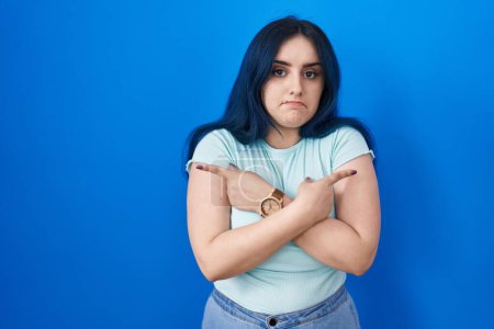 Photo for Young modern girl with blue hair standing over blue background pointing to both sides with fingers, different direction disagree - Royalty Free Image