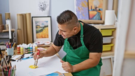 Photo for Confident young latin man artist, passionately drawing in his notebook at a bustling art studio, amidst the engaging hum of learning and creativity - Royalty Free Image