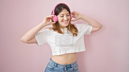 Téléchargez les photos : Jeune femme blonde écoutant de la musique et dansant sur fond rose isolé - en image libre de droit