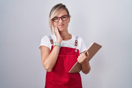 Photo for Young blonde woman wearing waiter uniform holding clipboard touching mouth with hand with painful expression because of toothache or dental illness on teeth. dentist concept. - Royalty Free Image