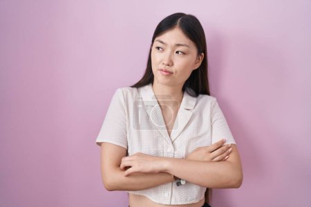 Téléchargez les photos : Chinois jeune femme debout sur fond rose regardant sur le côté avec les bras croisés convaincu et confiant - en image libre de droit