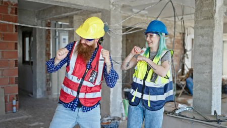 Téléchargez les photos : Hommes et femmes constructeurs souriant danse confiante sur le chantier de construction - en image libre de droit