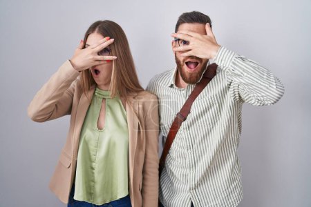 Photo for Young couple standing over white background peeking in shock covering face and eyes with hand, looking through fingers with embarrassed expression. - Royalty Free Image