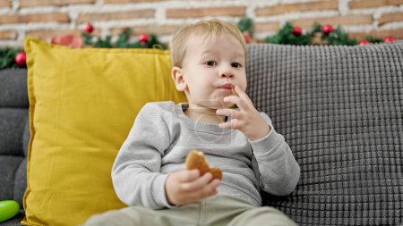 Photo for Caucasian toddler sitting on the sofa eating cookies at home - Royalty Free Image