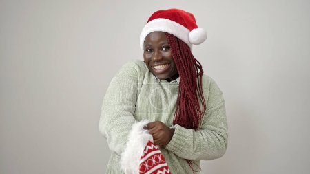 Photo for African woman with braided hair wearing christmas hat looking inside of sock over white background - Royalty Free Image