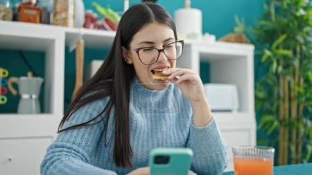 Téléchargez les photos : Jeune femme hispanique utilisant smartphone prendre le petit déjeuner à la salle à manger - en image libre de droit