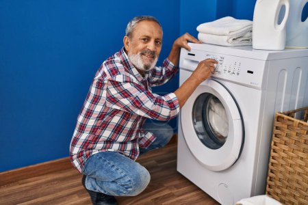 Photo for Senior grey-haired man smiling confident turning on washing machine at laundry room - Royalty Free Image