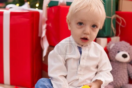 Téléchargez les photos : Adorable bambin blond assis sur le sol par des cadeaux de Noël à la maison - en image libre de droit
