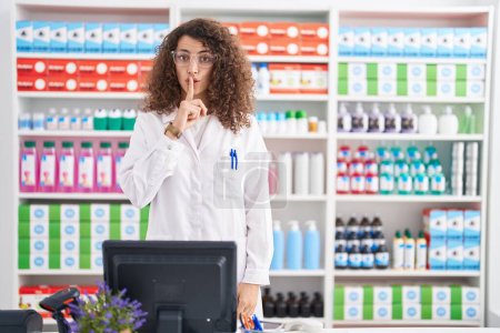 Photo for Hispanic woman with curly hair working at pharmacy drugstore asking to be quiet with finger on lips. silence and secret concept. - Royalty Free Image