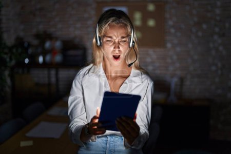 Téléchargez les photos : Jeune femme blonde travaillant au bureau la nuit dans le visage choqué, l'air sceptique et sarcastique, surprise avec la bouche ouverte - en image libre de droit