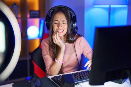 Téléchargez les photos : Jeune femme hispanique jouant à des jeux vidéo touchant la bouche avec la main avec une expression douloureuse à cause de maux de dents ou de maladies dentaires sur les dents. dentiste - en image libre de droit
