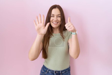 Téléchargez les photos : Belle femme brune debout sur fond rose montrant et pointant vers le haut avec les doigts numéro six tout en souriant confiant et heureux. - en image libre de droit