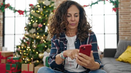 Téléchargez les photos : Moyen Age hispanique femme shopping avec smartphone et carte de crédit célébrant Noël à la maison - en image libre de droit