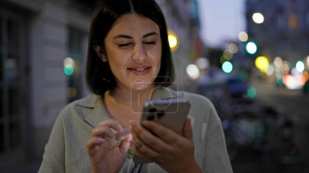 Photo for Young beautiful hispanic woman using smartphone in the streets at night - Royalty Free Image