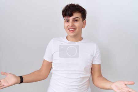 Téléchargez les photos : Jeune homme non binaire portant un t-shirt blanc décontracté souriant gai à bras ouverts comme accueil amical, salutations positives et confiantes - en image libre de droit