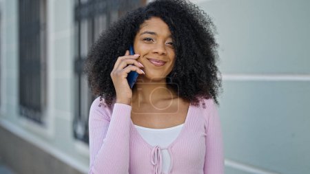 Téléchargez les photos : Afro-américaine femme souriant confiant parler sur le smartphone à la rue - en image libre de droit