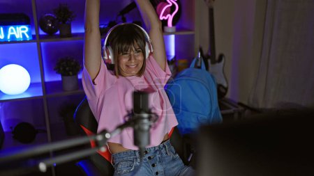 Photo for Confident hispanic female gamer, flashing a winner smile while streaming her night gaming session with a beautiful hairstyle and headset, in her home-office's indoor gaming room - Royalty Free Image