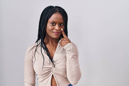Téléchargez les photos : Femme africaine avec des tresses debout sur fond blanc pointant vers l'oeil vous regardant geste, expression suspecte - en image libre de droit