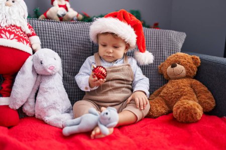 Photo for Adorable blond toddler sitting on sofa wearing christmas hat at home - Royalty Free Image