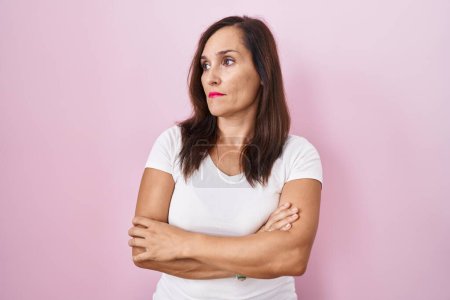 Téléchargez les photos : Moyen âge brunette femme debout sur fond rose regardant sur le côté avec les bras croisés convaincu et confiant - en image libre de droit