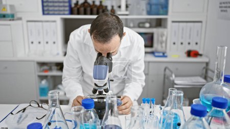 Téléchargez les photos : Homme âgé avec les cheveux gris, un scientifique occupé dans son laboratoire, regardant au microscope pour la découverte médicale - en image libre de droit