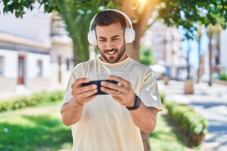 Téléchargez les photos : Jeune homme hispanique souriant confiant jouer au jeu vidéo au parc - en image libre de droit