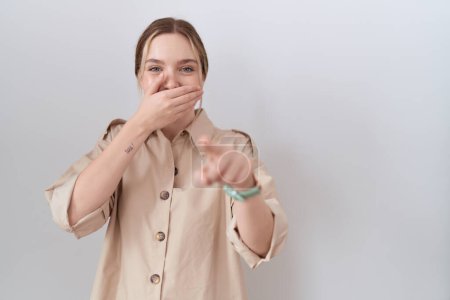 Foto de Mujer caucásica joven con camisa casual riéndose de ti, señalando con el dedo a la cámara con la mano sobre la boca, expresión de vergüenza - Imagen libre de derechos